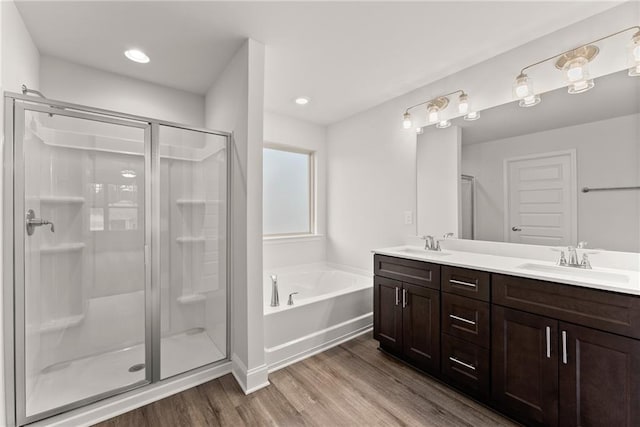 bathroom with a bath, a stall shower, a sink, and wood finished floors