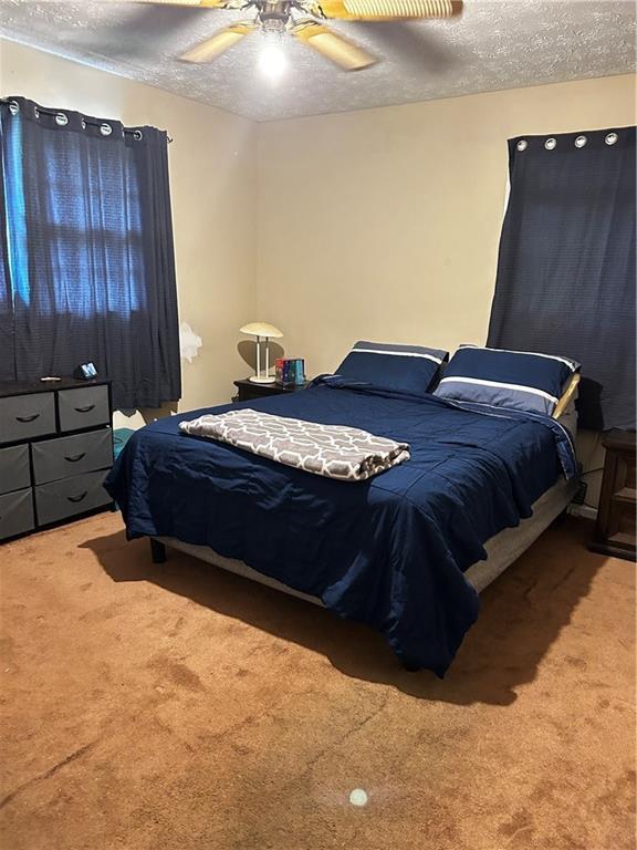 carpeted bedroom with ceiling fan and a textured ceiling