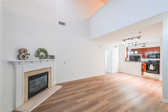 unfurnished living room with a towering ceiling, rail lighting, and light hardwood / wood-style floors