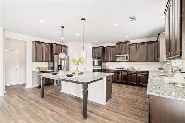 kitchen with a kitchen island, sink, backsplash, hanging light fixtures, and stainless steel appliances