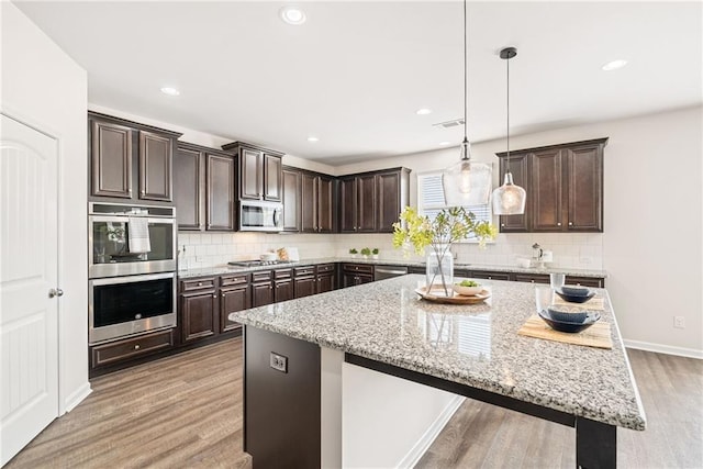 kitchen with pendant lighting, a kitchen bar, a center island, dark brown cabinetry, and stainless steel appliances