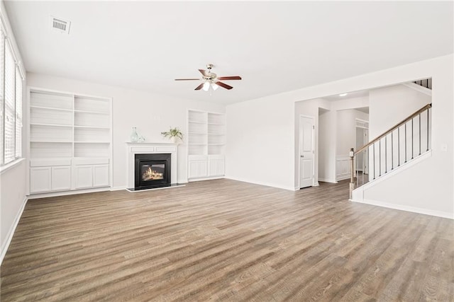 unfurnished living room featuring wood-type flooring, built in features, and ceiling fan