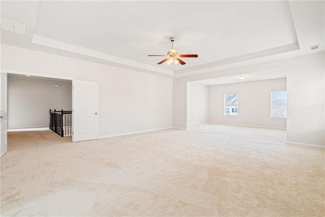 carpeted spare room with a tray ceiling and ceiling fan