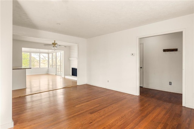 unfurnished living room with dark wood-style floors, ceiling fan, a brick fireplace, and baseboards