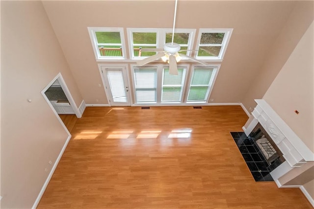 unfurnished living room with ceiling fan, light hardwood / wood-style floors, and a high ceiling