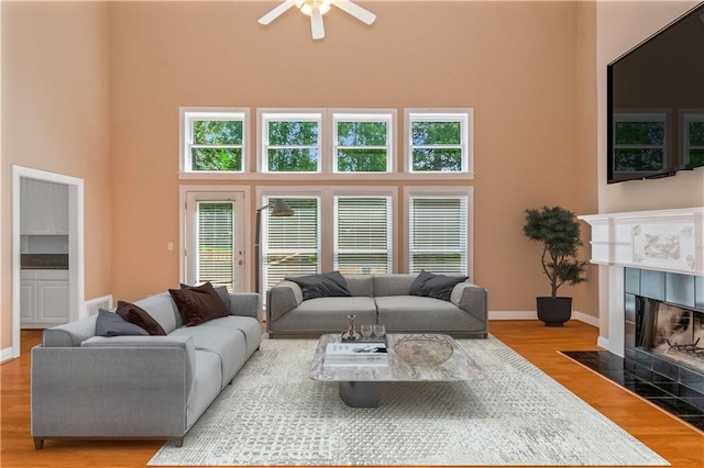 living room with a high ceiling, ceiling fan, light wood-type flooring, and a fireplace