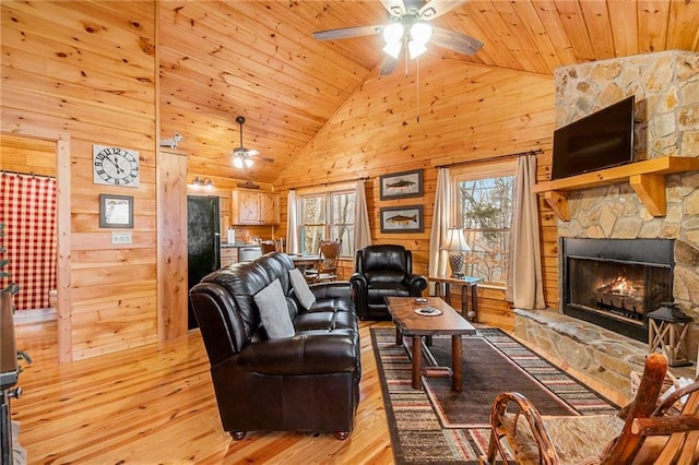 living room with ceiling fan, wood walls, a fireplace, wooden ceiling, and light wood-type flooring