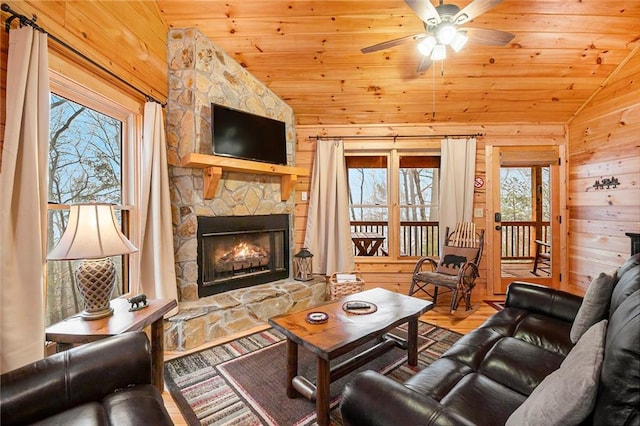 living room with wood ceiling, a stone fireplace, vaulted ceiling, and wooden walls