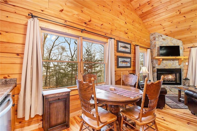 dining space featuring lofted ceiling, a stone fireplace, light hardwood / wood-style floors, and wood walls