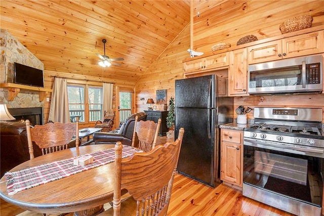 kitchen featuring a stone fireplace, vaulted ceiling, light hardwood / wood-style flooring, appliances with stainless steel finishes, and wooden walls