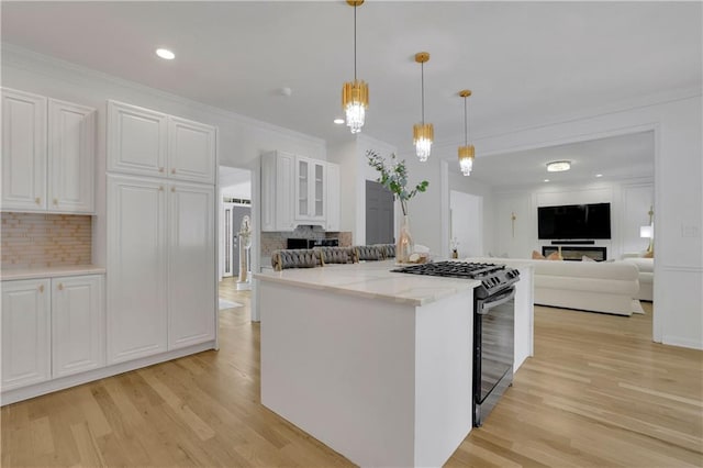 kitchen with light stone counters, light hardwood / wood-style floors, white cabinets, gas range, and decorative light fixtures