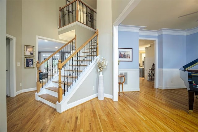 stairs with a towering ceiling, hardwood / wood-style flooring, and ornamental molding