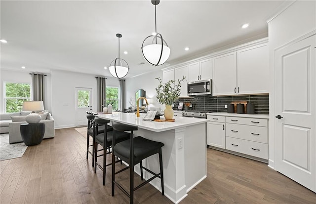 kitchen with a breakfast bar area, hardwood / wood-style flooring, open floor plan, backsplash, and stainless steel microwave