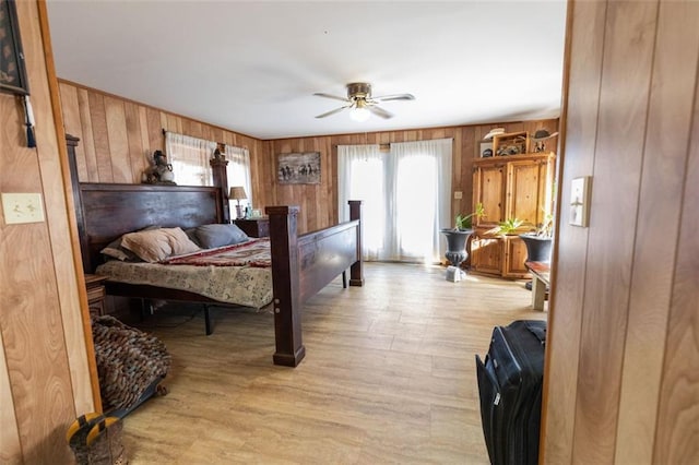 bedroom featuring ceiling fan, wood walls, multiple windows, and light hardwood / wood-style flooring