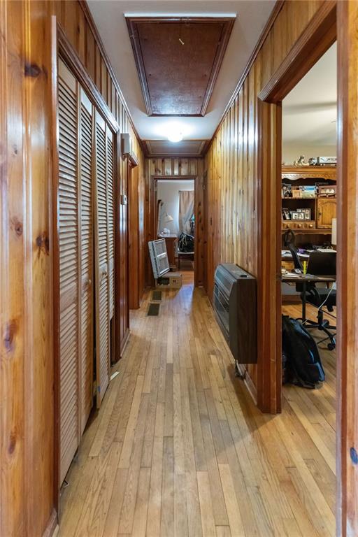 corridor featuring crown molding, wood walls, heating unit, and light wood-type flooring