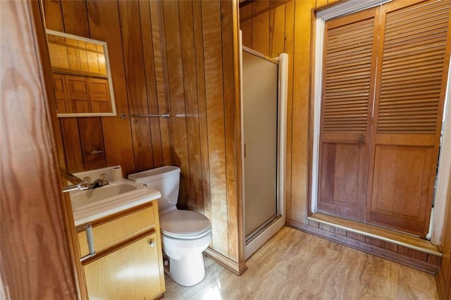 bathroom featuring vanity, a shower with shower door, wood walls, and toilet