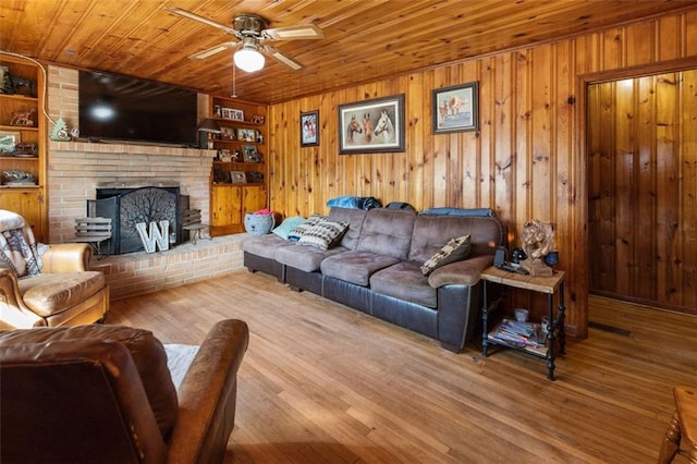 living room featuring ceiling fan, wooden walls, a brick fireplace, wooden ceiling, and light wood-type flooring