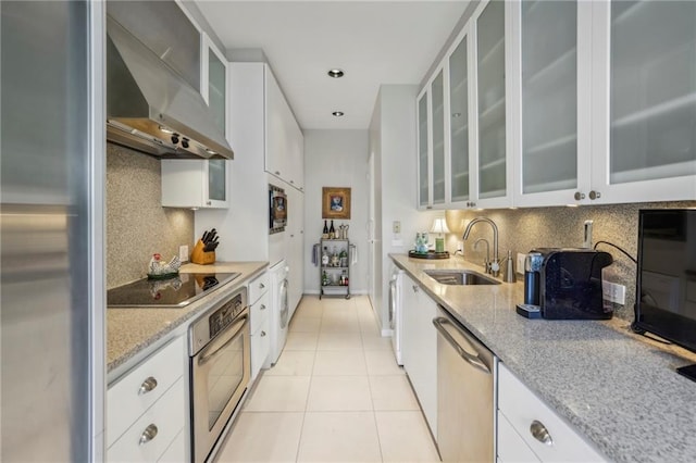 kitchen featuring appliances with stainless steel finishes, sink, wall chimney range hood, white cabinetry, and light tile patterned flooring