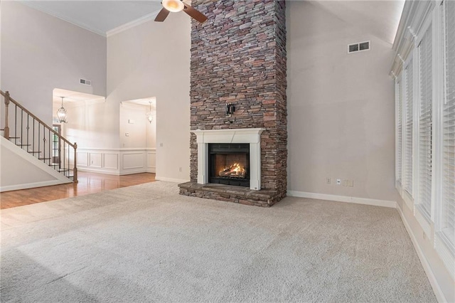 unfurnished living room featuring carpet flooring, a towering ceiling, ceiling fan, a fireplace, and stairs