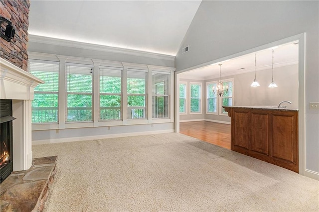 unfurnished living room featuring a lit fireplace, carpet, a chandelier, vaulted ceiling, and crown molding