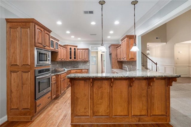 kitchen featuring appliances with stainless steel finishes, brown cabinetry, ornamental molding, a breakfast bar, and a peninsula