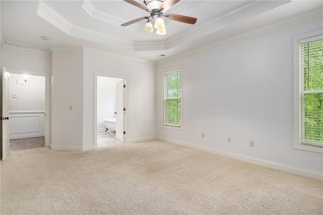 unfurnished bedroom featuring light carpet, a tray ceiling, ornamental molding, ensuite bathroom, and baseboards