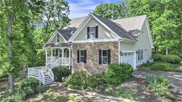 view of front of property featuring stone siding, a porch, asphalt driveway, an attached garage, and stairway