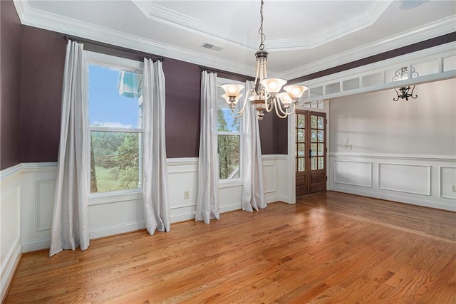 unfurnished dining area with a chandelier, light wood finished floors, a wainscoted wall, a raised ceiling, and a decorative wall