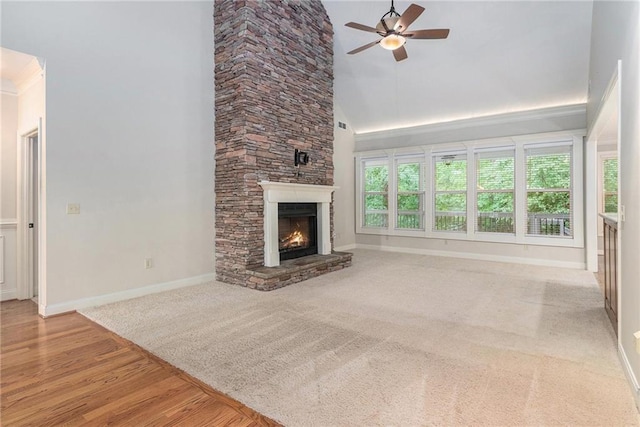 unfurnished living room with ceiling fan, baseboards, a stone fireplace, high vaulted ceiling, and carpet