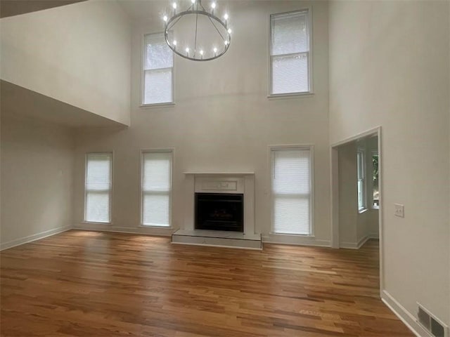 unfurnished living room with hardwood / wood-style floors, a towering ceiling, and a notable chandelier