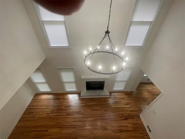 unfurnished living room with plenty of natural light, dark hardwood / wood-style flooring, a towering ceiling, and a chandelier