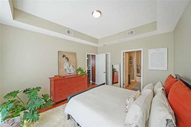 bedroom featuring a tray ceiling, hardwood / wood-style floors, and ensuite bathroom