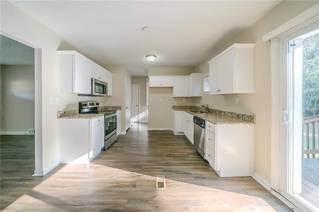 kitchen with stainless steel appliances, sink, white cabinets, and light stone counters