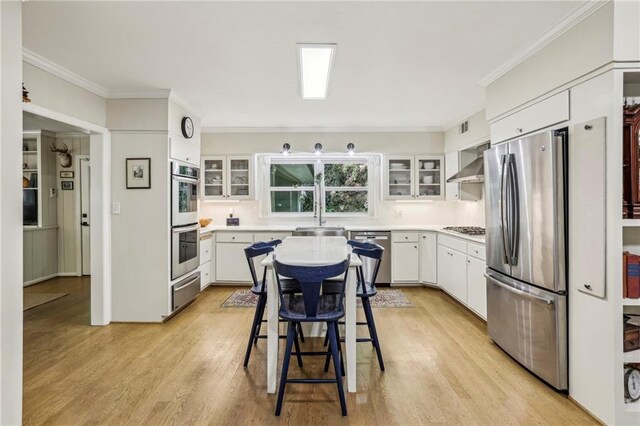 3311 Stillhouse Rd SE, Atlanta, GA 30339 - kitchen featuring stainless steel appliances, light wood-style flooring, ornamental molding, light countertops, and wall chimney range hood