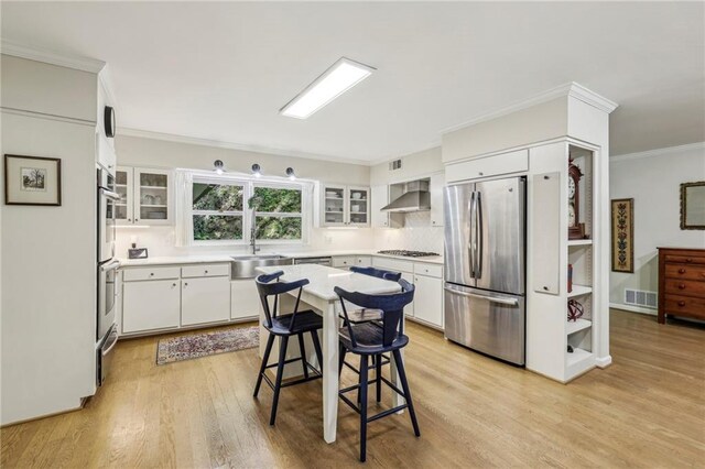 3311 Stillhouse Rd SE, Atlanta, GA 30339 - kitchen featuring appliances with stainless steel finishes, light wood finished floors, wall chimney exhaust hood, crown molding, and white cabinetry