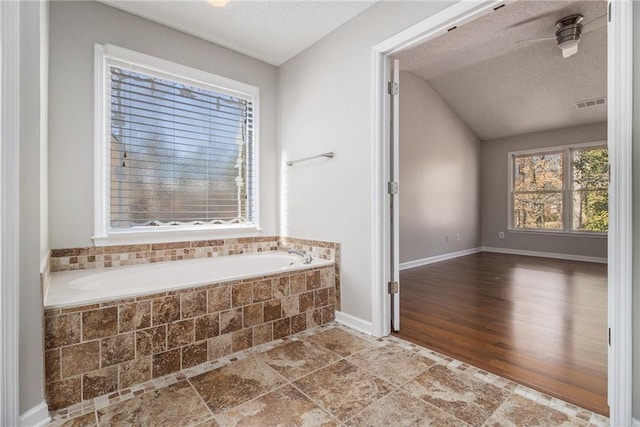 bathroom with a relaxing tiled tub, vaulted ceiling, and a textured ceiling