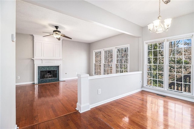 unfurnished living room featuring hardwood / wood-style flooring, a high end fireplace, and ceiling fan with notable chandelier