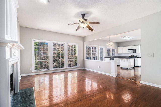 unfurnished living room with ceiling fan with notable chandelier, dark hardwood / wood-style floors, and a textured ceiling