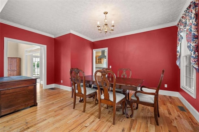 dining space with a textured ceiling, light hardwood / wood-style floors, an inviting chandelier, and crown molding