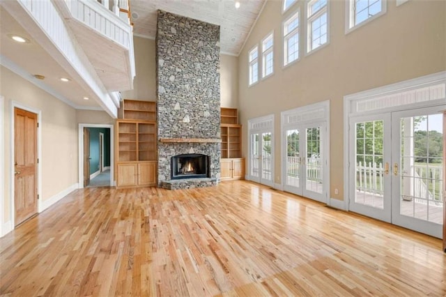 unfurnished living room featuring light wood-type flooring, high vaulted ceiling, a stone fireplace, and built in shelves