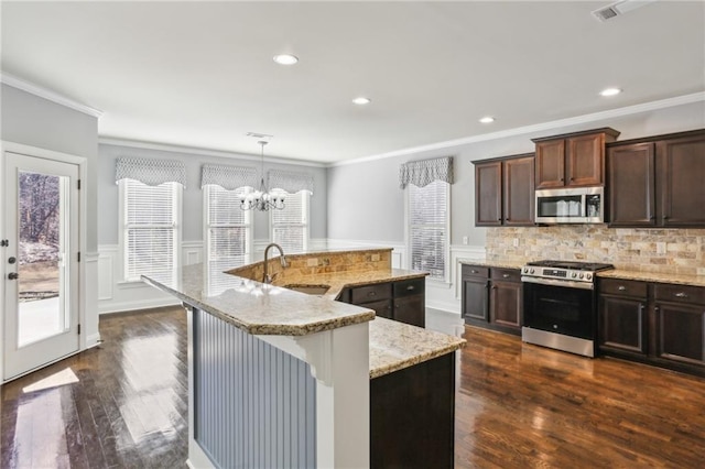 kitchen featuring appliances with stainless steel finishes, sink, hanging light fixtures, dark brown cabinets, and a kitchen island with sink