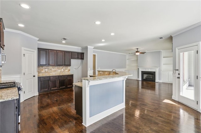 kitchen featuring dark brown cabinets, a kitchen island with sink, light stone countertops, and gas stove