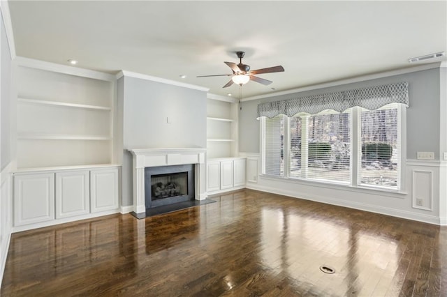 unfurnished living room with built in features, ceiling fan, crown molding, and dark hardwood / wood-style flooring