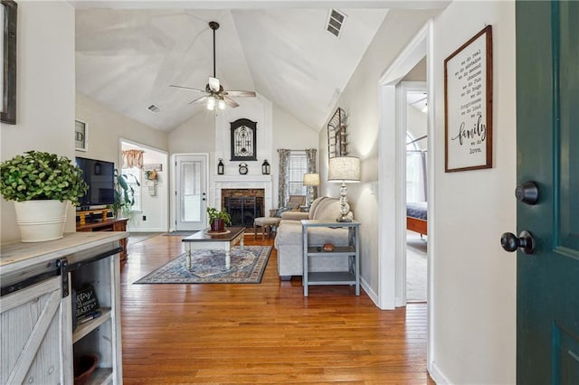 living room featuring ceiling fan, a stone fireplace, vaulted ceiling, and light hardwood / wood-style flooring