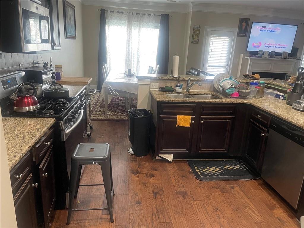 kitchen featuring appliances with stainless steel finishes, sink, light stone countertops, hardwood / wood-style floors, and dark brown cabinetry