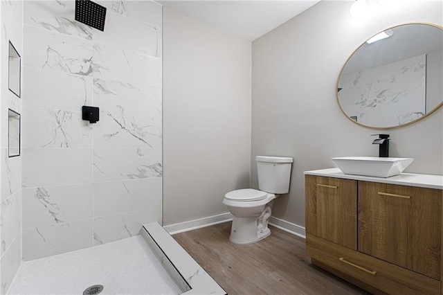 bathroom featuring hardwood / wood-style flooring, vanity, toilet, and a tile shower