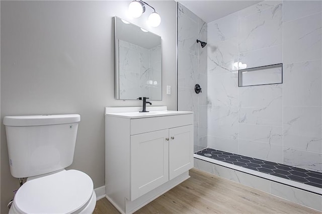 bathroom with hardwood / wood-style flooring, vanity, a tile shower, and toilet