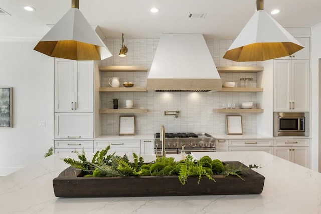 kitchen with premium range hood, appliances with stainless steel finishes, light stone counters, and white cabinets