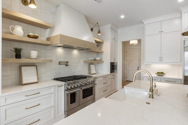 kitchen with premium range hood, white cabinetry, sink, stainless steel appliances, and light stone countertops