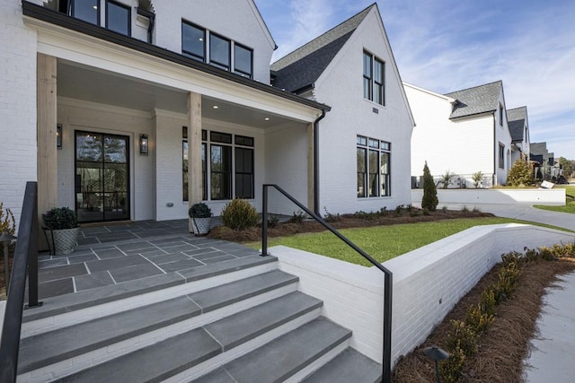 view of exterior entry with covered porch and a lawn